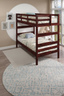 Wooden bunk bed with patterned bedding in a cozy, light-filled bedroom. Animal art hangs on the wall, and a round rug covers the floor. A window allows natural light into the room.