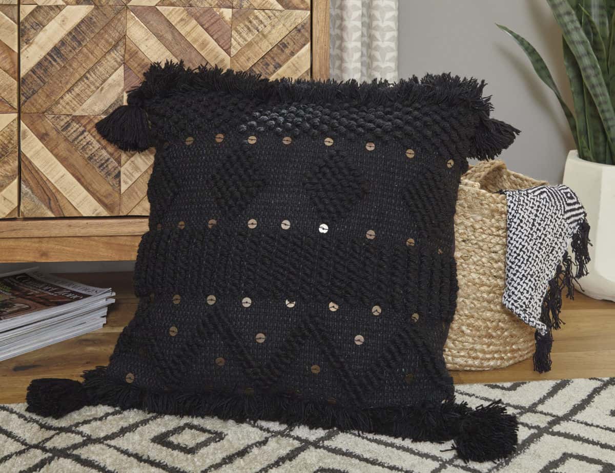 A1000934 Mordechai Pillow Room picture of a textured black ground is highlighted with goldtone accents and tassels on each corner of the pillow.