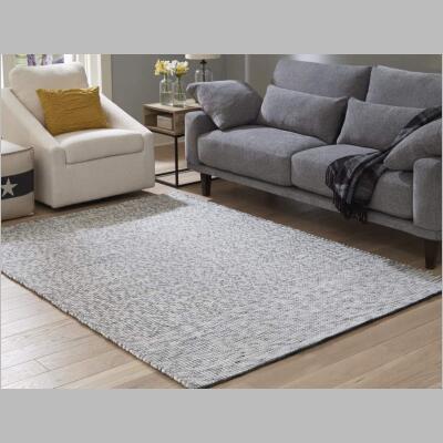 The Jonalyn rug pictured in a room, has a raised stitched, with a gray and charcoal palette. Designed to fit into many interiors.